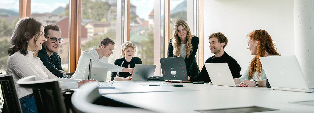 Sieben Personen arbeiten versammelt um einen Tisch an ihren Laptops und besprechen Dinge miteinander. | © FH Kufstein Tirol