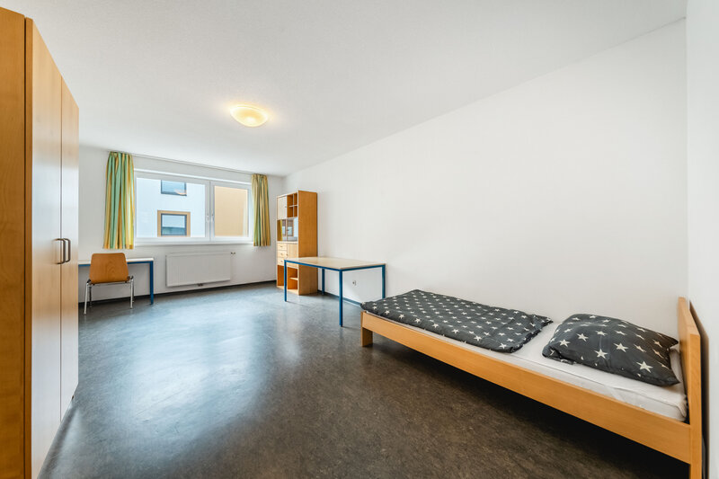 Ein großes Zimmer mit einem Schrank und zwei Tischen. Außerdem gibt es ein großes Fenster und rechts daneben ein Regal. | © FH Kufstein Tirol