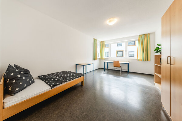 Haus_C_Doppelstudio_Gross_Schlafzimmer2_1 | © FH Kufstein Tirol Ein ordentlich eingerichtetes, gut beleuchtetes Zimmer. Links steht ein Einzelbett. Vor dem Bett steht ein kleiner Tisch mit zwei Stühlen. Neben dem Bett rechts befindet sich ein großer Schrank. | © FH Kufstein Tirol