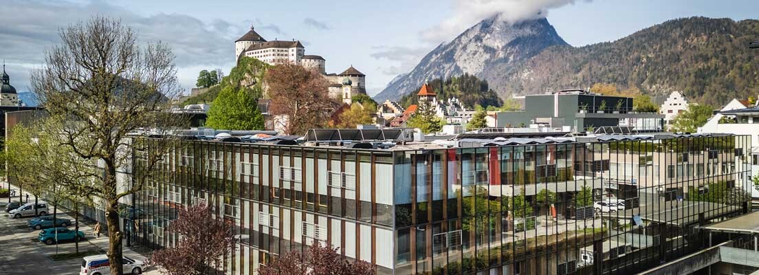 Moderne Hochschulgebäude mit Glasfassade, im Hintergrund die Festung Kufstein und der Pendling