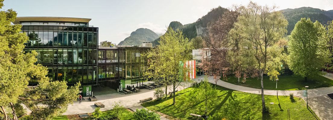 Panoramaaufnahme des Campus der FH Kufstein Tirol mit moderner Glasfassade, Grünflächen und Bergkulisse