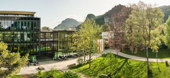 Panoramaaufnahme des Campus der FH Kufstein Tirol mit moderner Glasfassade, Grünflächen und Bergkulisse