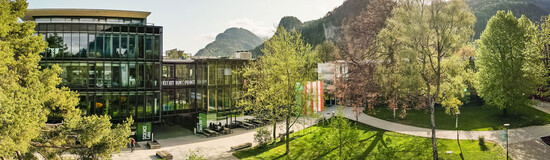 Panoramaaufnahme des Campus der FH Kufstein Tirol mit moderner Glasfassade, Grünflächen und Bergkulisse