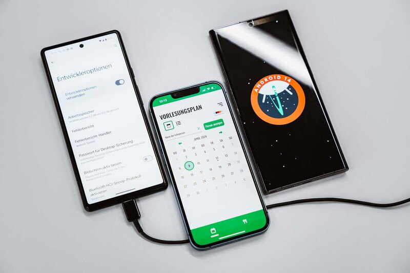 Drei Smartphones mit Android-Entwickleroptionen, Stundenplan-App und Android-14-Logo im Web Lab der FH Kufstein Tirol.