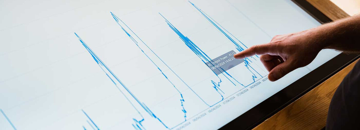 Finger zeigt auf Energiediagramm mit Leistungsdaten auf Touchscreen im Sustain & Estate Lab der FH Kufstein Tirol.