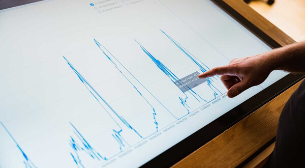 Finger zeigt auf Energiediagramm mit Leistungsdaten auf Touchscreen im Sustain & Estate Lab der FH Kufstein Tirol.