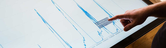 Finger zeigt auf Energiediagramm mit Leistungsdaten auf Touchscreen im Sustain & Estate Lab der FH Kufstein Tirol.