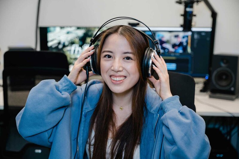 Studentin im Media Lab der FH Kufstein Tirol arbeitet mit Kopfhörern an einer Audioproduktion und lächelt in die Kamera.