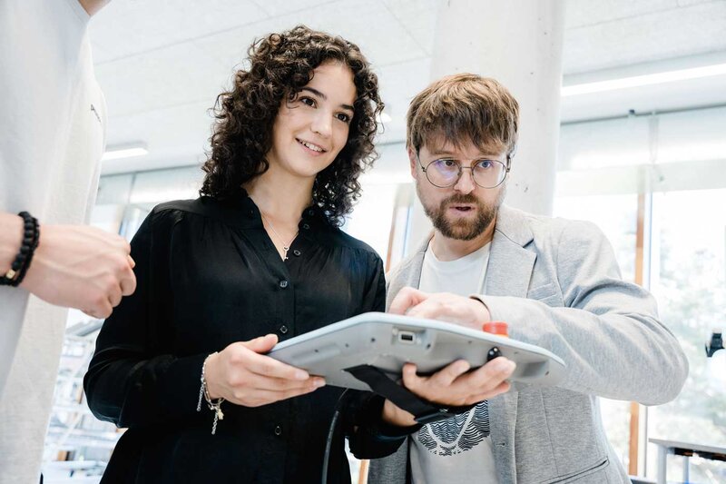 Zwei Personen steuern eine industrielle Automatisierungsanlage über ein Tablet im Labor.