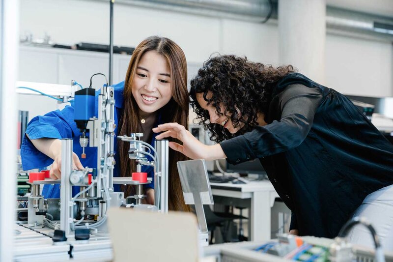 Zwei Studierende arbeiten gemeinsam an einer automatisierten Fertigungsanlage im Automation Lab der FH Kufstein Tirol.
