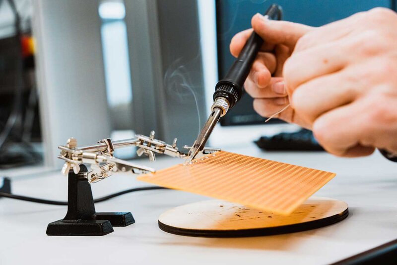 Nahaufnahme einer Lötstation, an der elektronische Bauteile auf eine Platine gelötet werden.