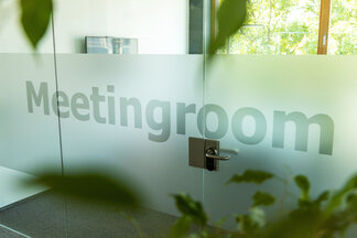 Verglaste Tür mit Meetingroom-Beschriftung und Pflanzen im Vordergrund