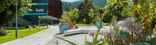 Blumenbeet im Vordergrund und das KUBI-Gebäude der FH Kufstein Tirol im Hintergrund an einem sonnigen Tag