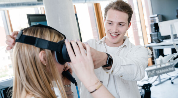 Digitalexperience_Lab_3D_Brille_Demonstration | © FH Kufstein Tirol Ein Mann hilft einer Frau, ein Virtual-Reality-Brille aufzusetzen. | © FH Kufstein Tirol