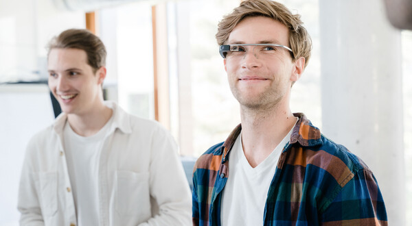 Digitalexperience_Lab_2_Personen.jpg | © FH Kufstein Tirol Zwei Männer in einem hellen Raum. Der vordere trägt eine Eye-Tracking Brille und ein kariertes Hemd, der hintere ein weißes Hemd und lächelt. | © FH Kufstein Tirol