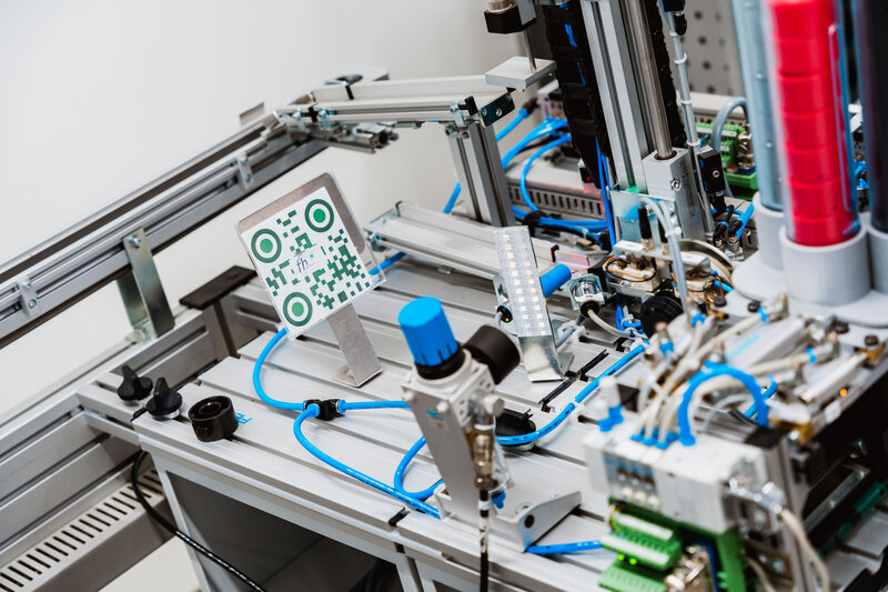 Automatisiertes Testsystem mit Sensoren, Ventilen und einem QR-Code-Schild auf dem Arbeitstisch.
