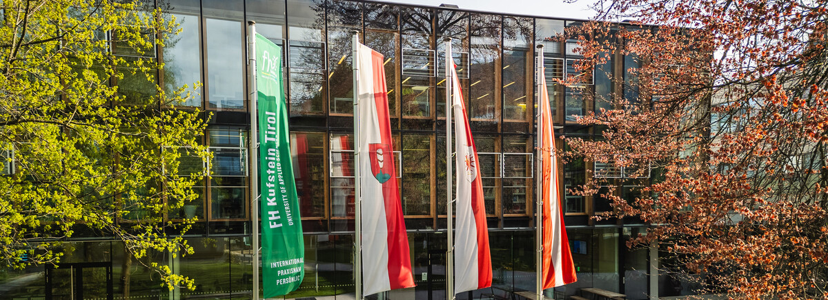 Profil_Organisation_Anker_2 | © FH Kufstein Tirol Der Park und das Gebäude der FH Kufstein Tirol, vor welcher 4 Flaggen errichtet sind. | © FH Kufstein Tirol