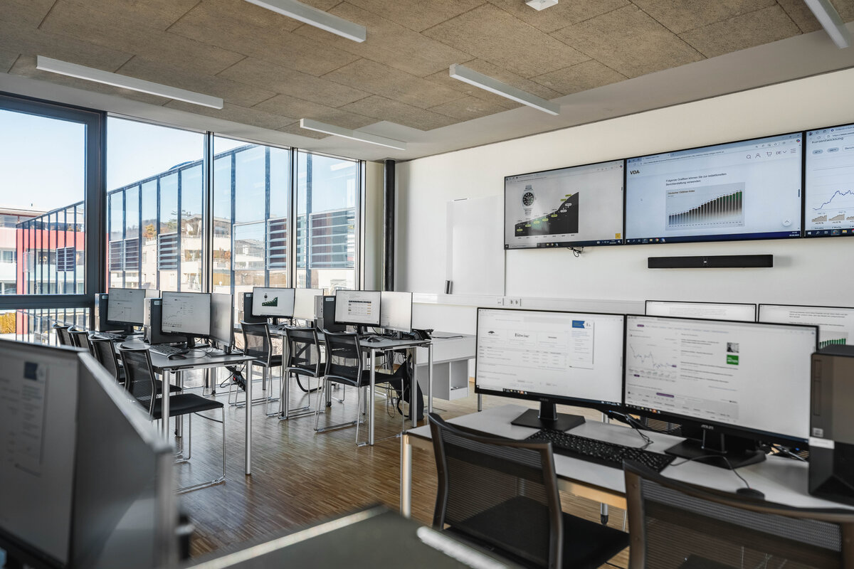Finance Lab Raumansicht 2 | © FH Kufstein Tirol Ein lichtdurchfluteter Computerraum mit Monitoren und Computerarbeitsplätzen; aus den Fenster sieht man ein weiteres Gebäude | © FH Kufstein Tirol