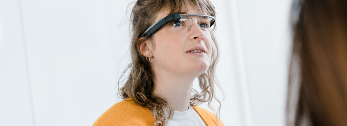 Digitalexperience_Lab_Frau_mit_Brille | © FH Kufstein Tirol Eine Frau mit brünetten, lockigen Haaren trägt eine Eye-Tracking Brille und schaut leicht nach oben. | © FH Kufstein Tirol