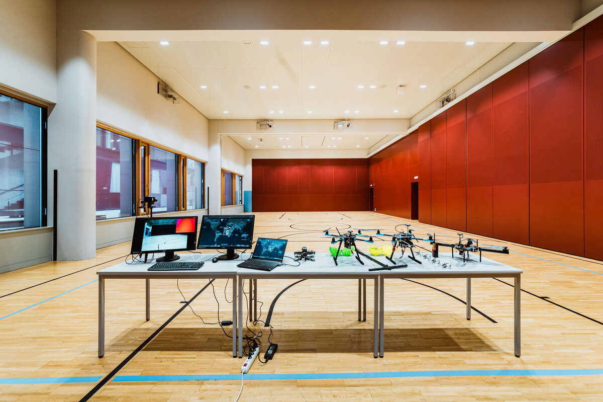 Drone_Lab_Drohnentechnologie-Setup.jpg | © FH Kufstein Tirol In der Mitte des Raumes befindet sich ein Tisch mit einer Vielzahl elektronischer Geräte, einschließlich eines Laptops, Monitoren und mehrerer Drohnen, die alle miteinander verbunden sind. | © FH Kufstein Tirol