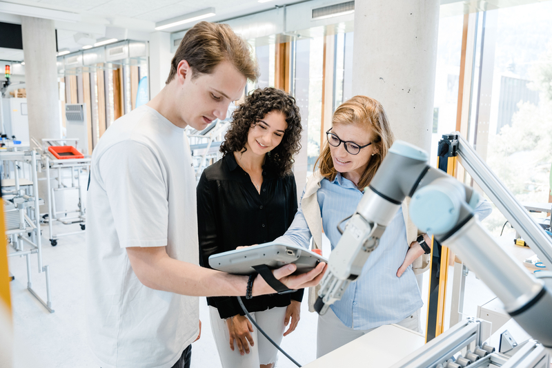 LEAN_Lab_Demonstration | © FH Kufstein Tirol Drei Personen schauen zusammen auf einen tragbaren Bildschirm, der von einem Mann gehalten wird. | © FH Kufstein Tirol