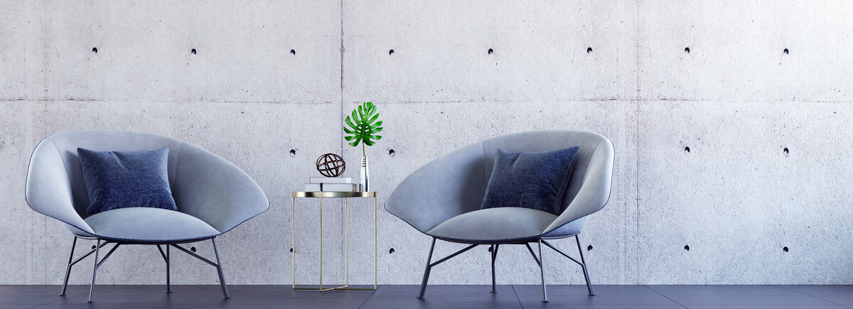 Master Lounge | © AdobeStock.teeraphan Zwei moderne Loungesessel stehen vor einer grauen Betonwand, zwischen ihnen ein moderner Tisch mit Dekoelementen | © AdobeStock.teeraphan
