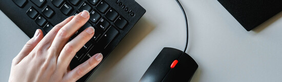 Hand tippt auf Tastatur neben Computermaus an modernem Arbeitsplatz