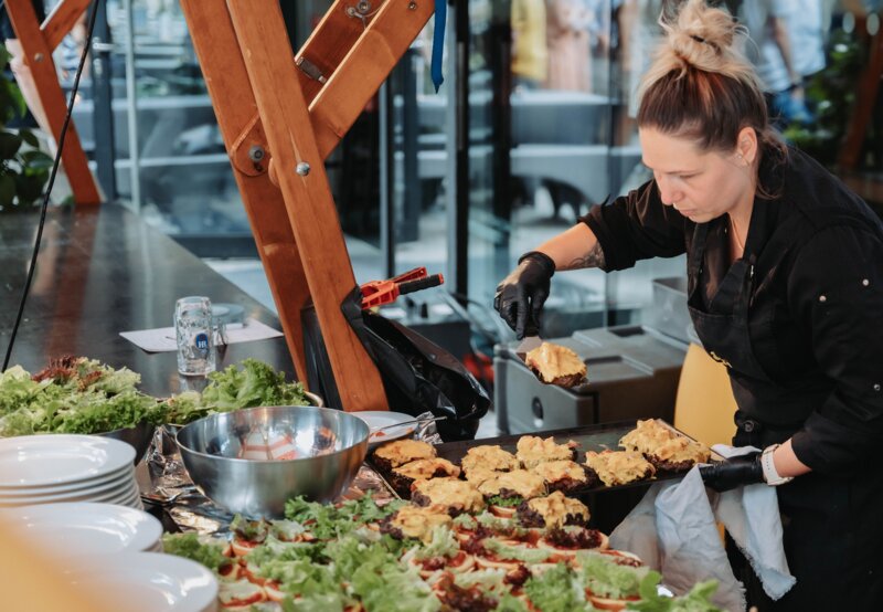 In schwarzer Berufskleidung arbeitet die Catering-Mitarbeiterin am Burger-Station. 