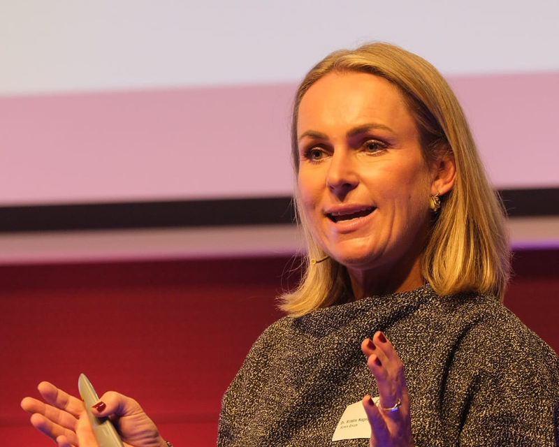 Kristin Nagel als Speakerin auf der hell beleuchteten Bühne beim 14. Internationalen Symposium Restrukturierung