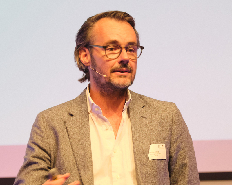 Thomas Schmid als Speaker auf der hell beleuchteten Bühne beim 14. Internationalen Symposium Restrukturierung