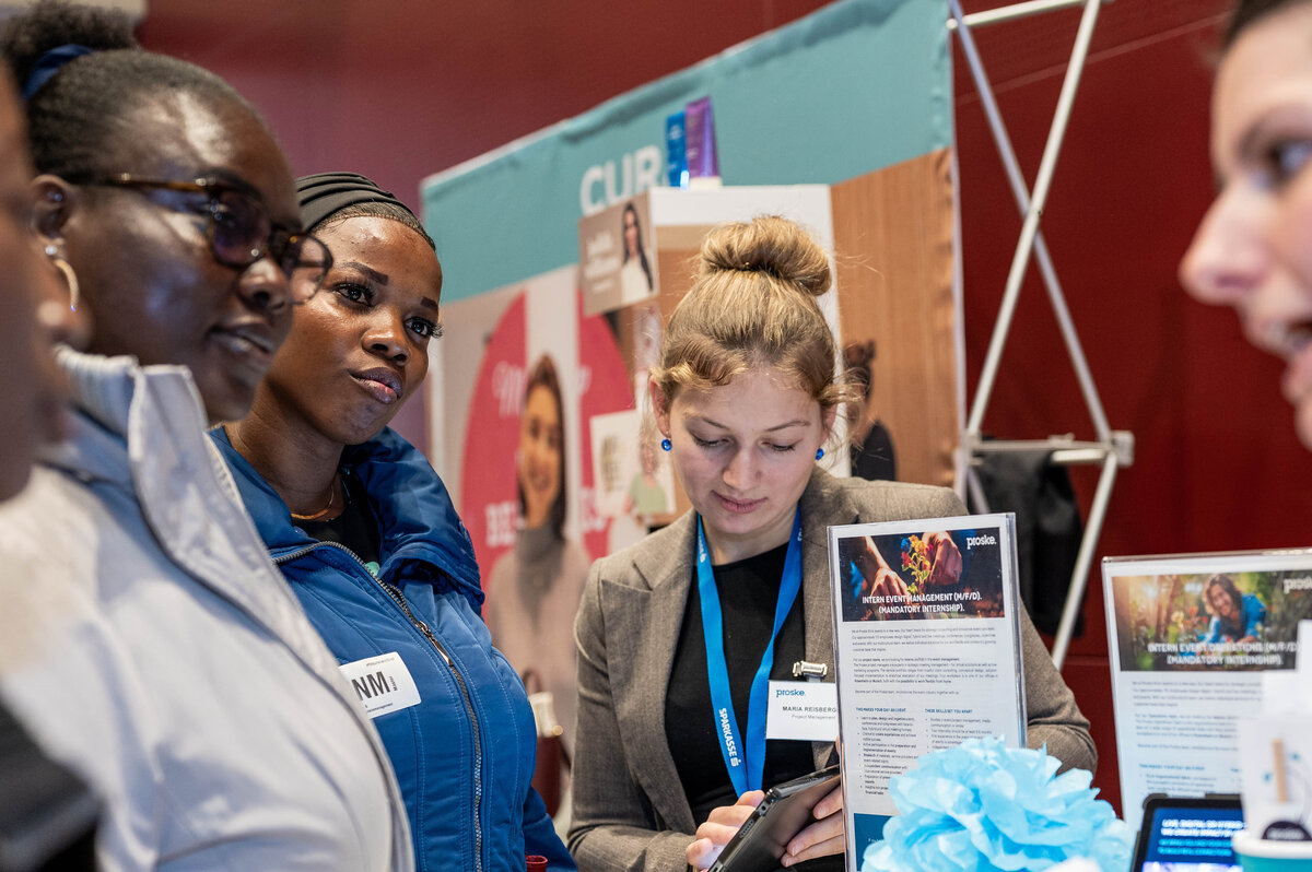 Gruppe von Besucherinnen informiert sich bei einem Beratungsstand auf der Meet & Match Karrieremesse.
