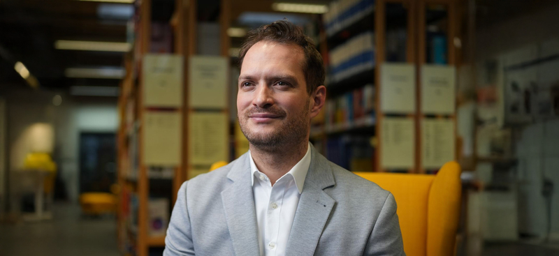 Prof. Dr. Maximilian Wolf sitzend vor einem Bücherregal.