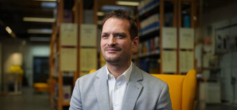 Prof. Dr. Maximilian Wolf sitzend vor einem Bücherregal.