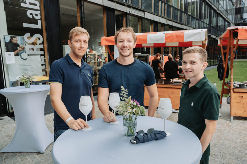 event-homecoming-besucher-stehtische-bereich-makers-lab-2025 | © FH Kufstein Tirol Homecoming-Teilnehmer drehen sich für einen spontanen Schnappschuss zur Kamera. | © FH Kufstein Tirol