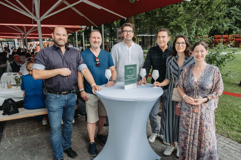 event-homecoming-gruppenfoto-stehtisch-2025 | © FH Kufstein Tirol Mehrere Gäste stellen sich lächelnd in Zweierreihen für das Foto auf. | © FH Kufstein Tirol