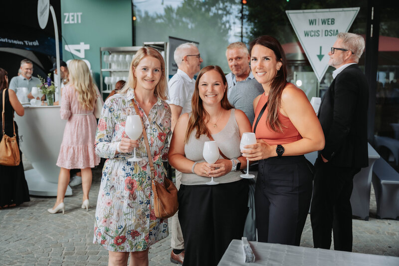 event-homecoming-gruppenbild-aussenbereich-2025 | © FH Kufstein Tirol Drei Gästinnen unterbrechen ihr Gespräch, um gemeinsam in die Kamera zu lächeln. | © FH Kufstein Tirol