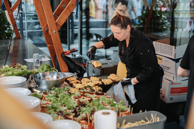 event-homecoming-mitarbeitende-gastrobereich-2025 | © FH Kufstein Tirol In schwarzer Berufskleidung arbeitet die Catering-Mitarbeiterin am Burger-Station. | © FH Kufstein Tirol