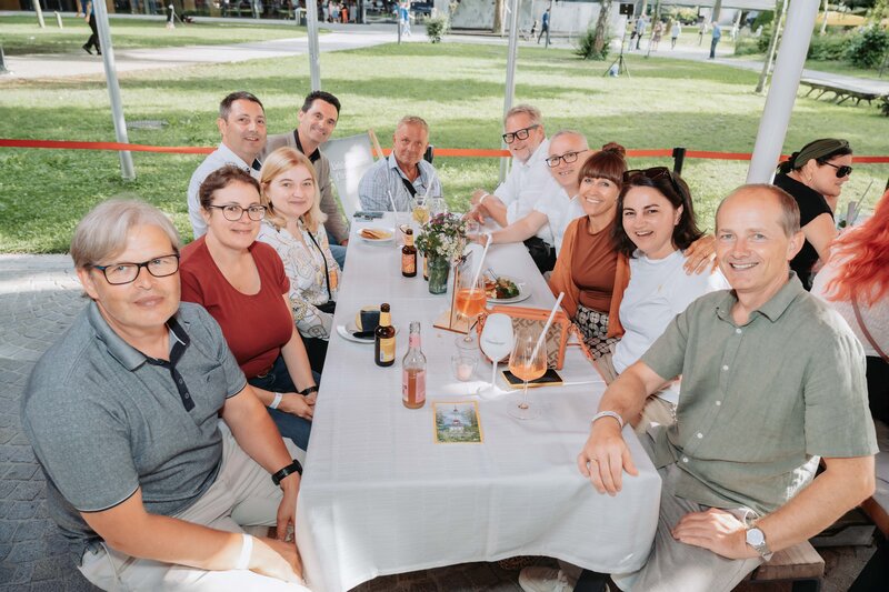 event-homecoming-personen-tischbereich-2025 | © FH Kufstein Tirol Eine Gruppe lacht gemeinsam in die Kamera. | © FH Kufstein Tirol