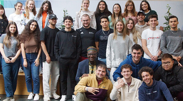 International_3 | © FH Kufstein Tirol Eine Gruppe von Studierenden der FH Kufstein Tirol steht und sitzt lächelnd zusammen mit Gastlektor Bella Bello Bitugu in der Aula der Fachhochschule Kufstein Tirol. | © FH Kufstein Tirol