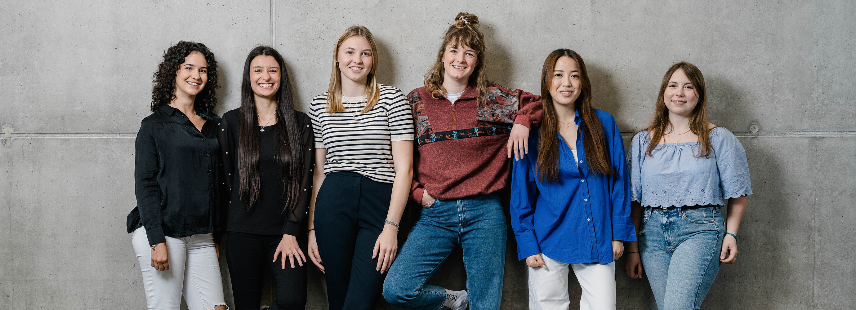 Gruppe von Studentinnen der FH Kufstein Tirol steht gemeinsam vor einer Betonwand und lächelt in die Kamera. | © FH Kufstein Tirol