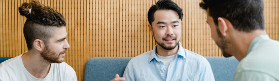 Drei Studierende im Gespräch bei Gruppenarbeit mit Laptop in moderner Sitzecke