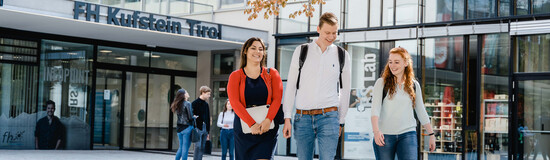 Drei Studierende der FH Kufstein Tirol gehen über den Campus vor dem Haupteingang der Hochschule.