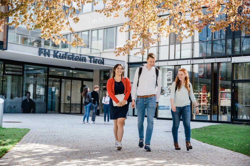 Drei Studierende der FH Kufstein Tirol gehen über den Campus vor dem Haupteingang der Hochschule.