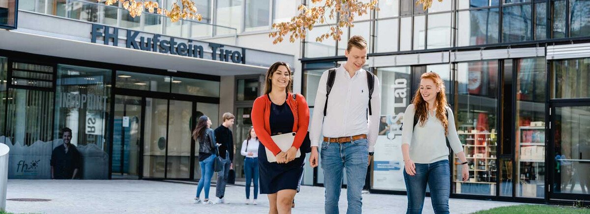 Drei Studierende der FH Kufstein Tirol gehen über den Campus vor dem Haupteingang der Hochschule.