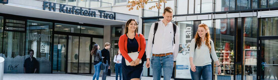 Drei Studierende der FH Kufstein Tirol gehen über den Campus vor dem Haupteingang der Hochschule.