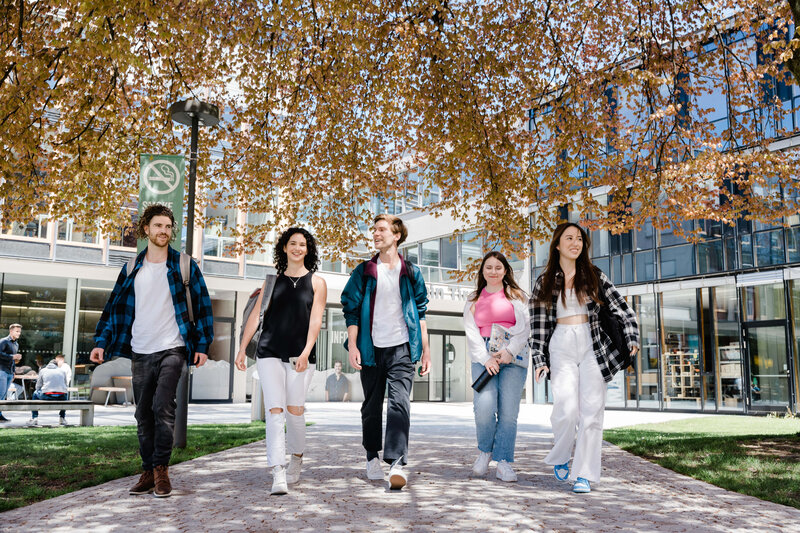 Fünf Studierende gehen gemeinsam über den Campus bei Frühlingswetter