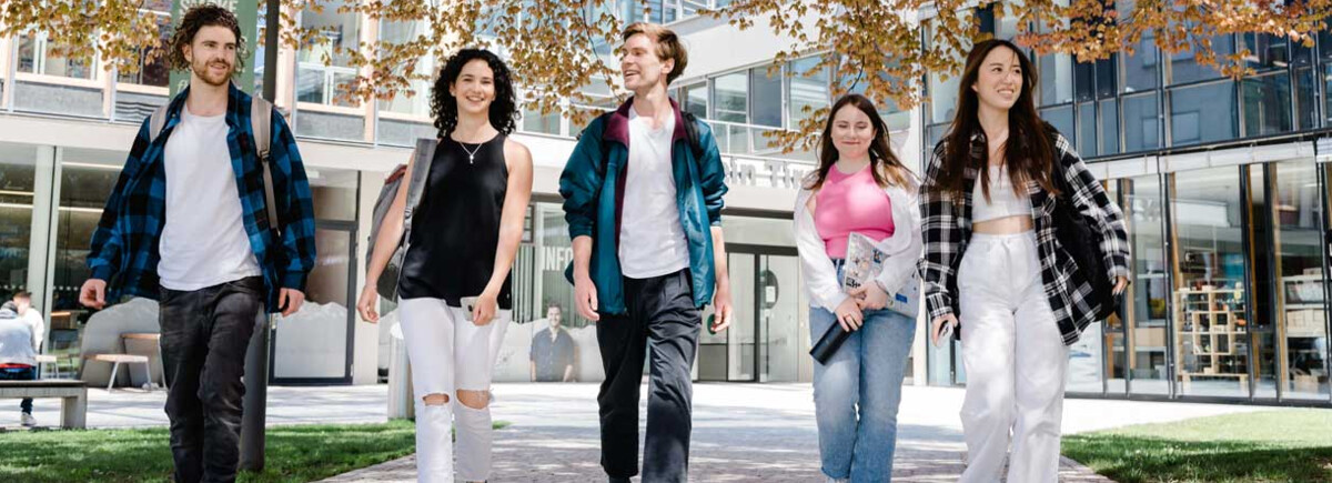 Fünf Studierende gehen gemeinsam über den Campus bei Frühlingswetter