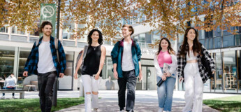 Fünf Studierende gehen gemeinsam über den Campus bei Frühlingswetter