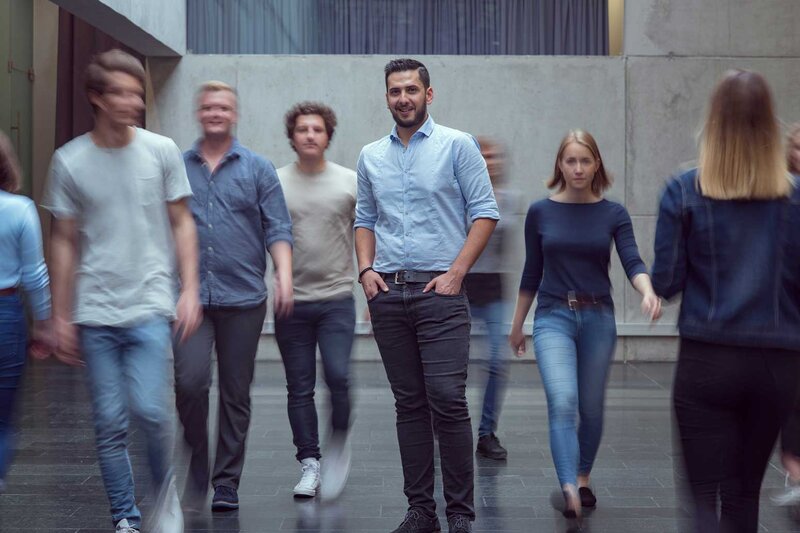 Viele Personen bewegen sich durch die Aula der FH Kufstein Tirol, und im Zentrum des Bildes steht ein Mann und blickt in die Kamera.