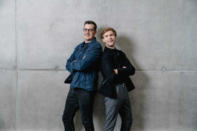 Zwei Studierende der FH Kufstein Tirol stehen entspannt vor einer Betonwand und blicken in die Kamera.